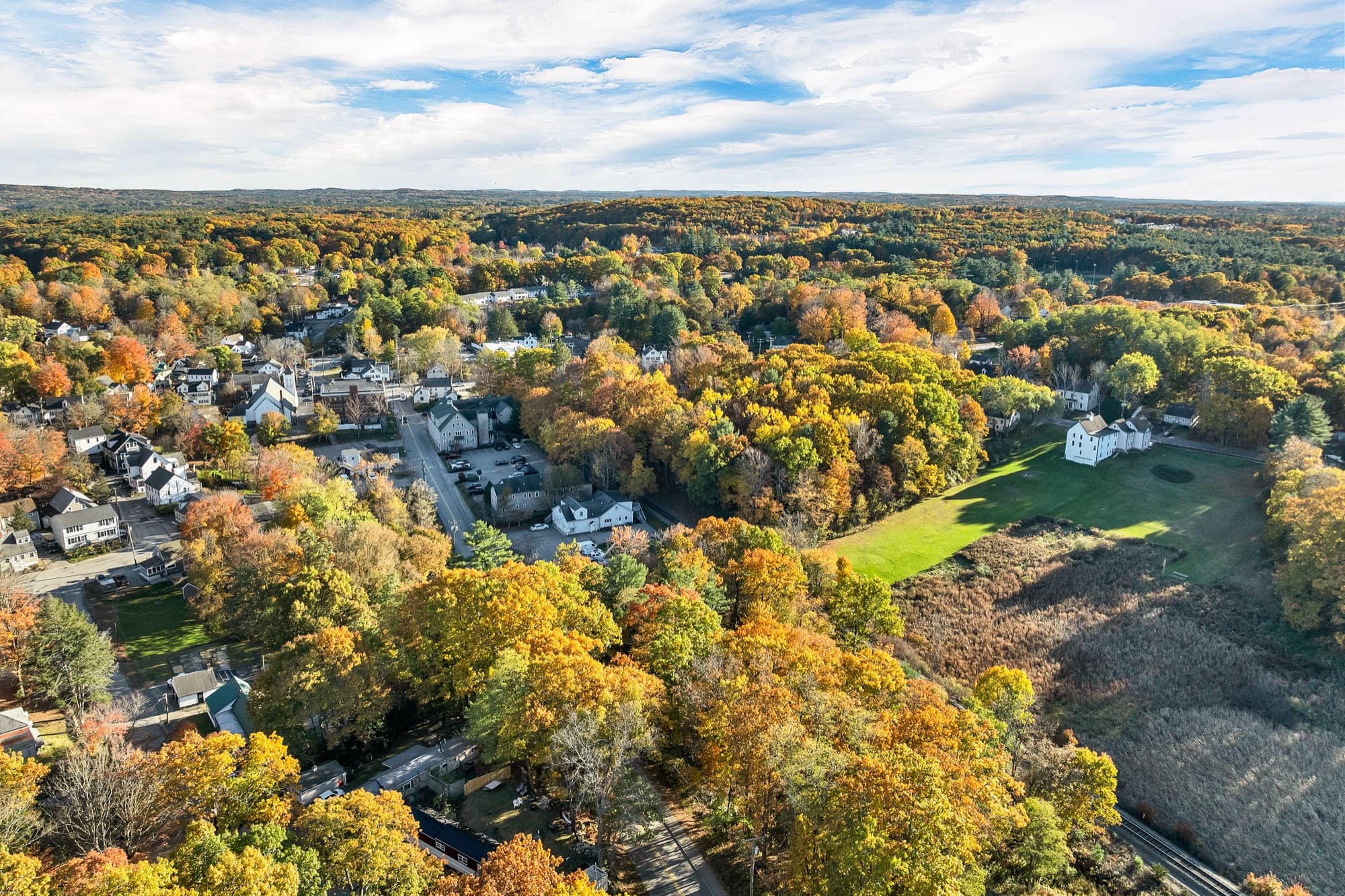 The village and a green field from the air, with the rail line along the woods