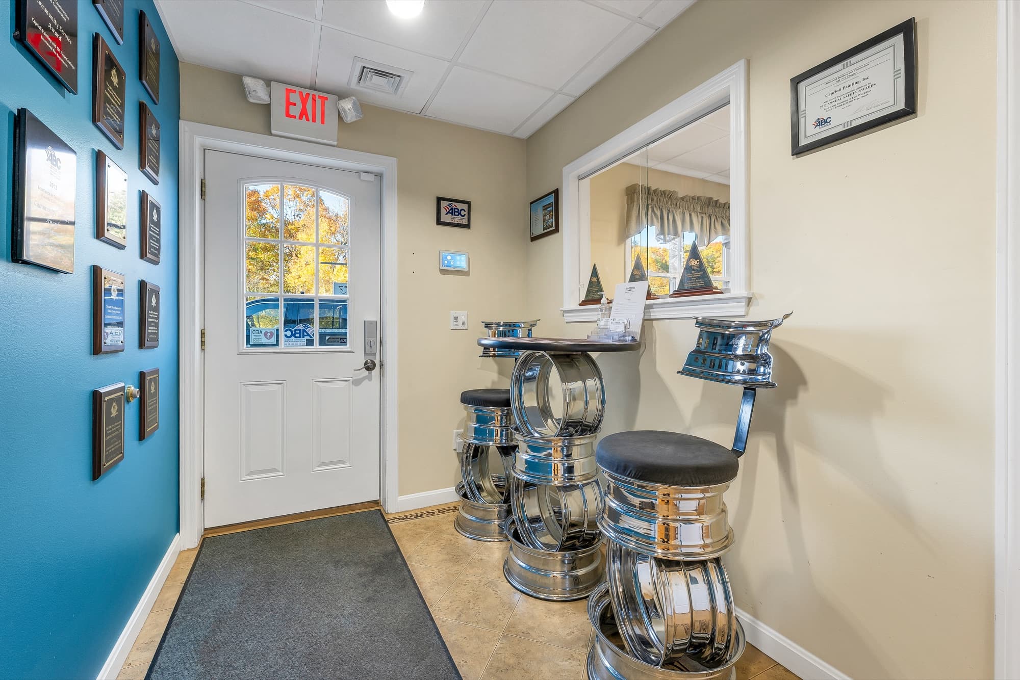 The office foyer with the entry door, a teal wall of plaques, and a window into the next office