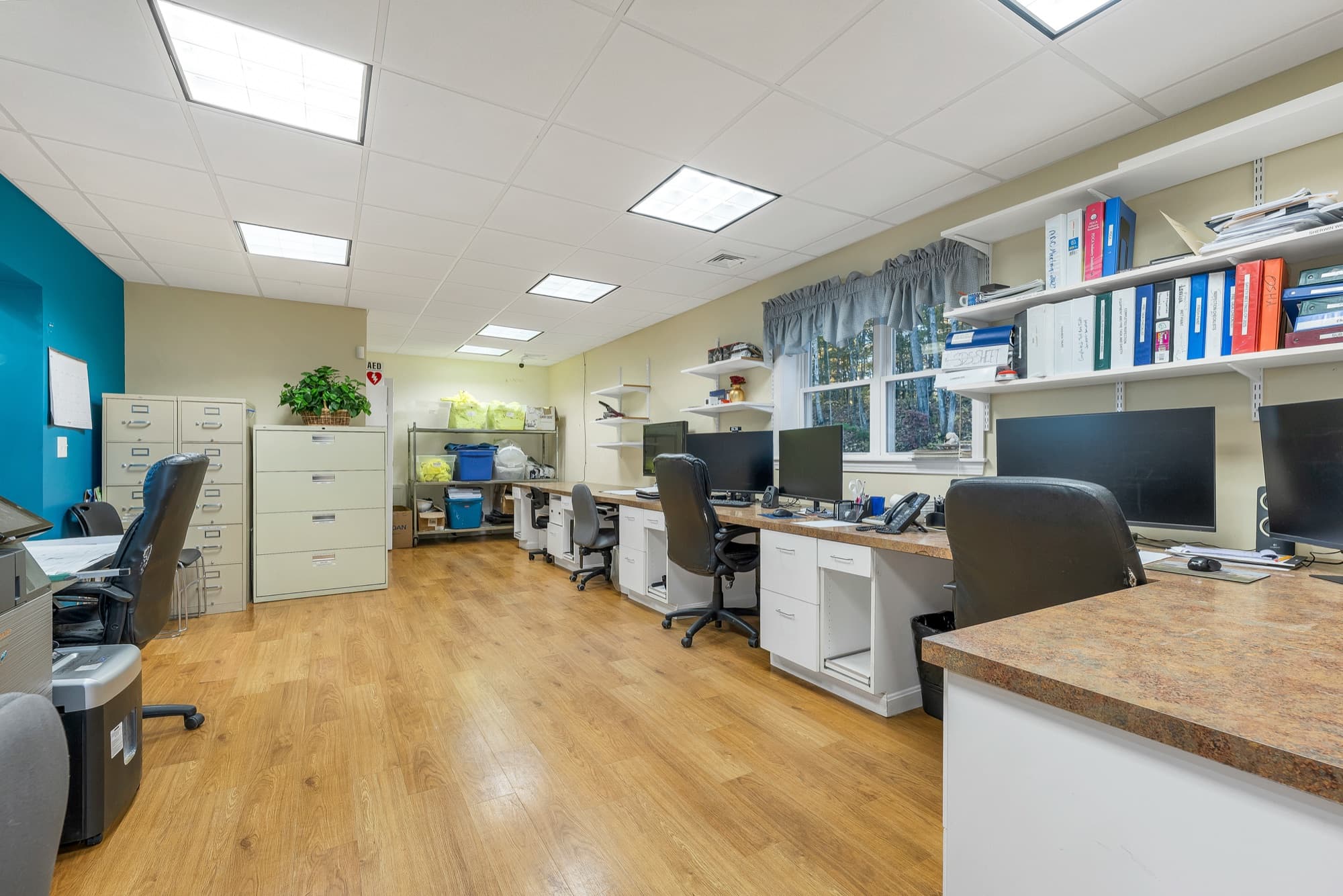 The open office with built-in desks along both walls, file cabinets, and a wood-look floor
