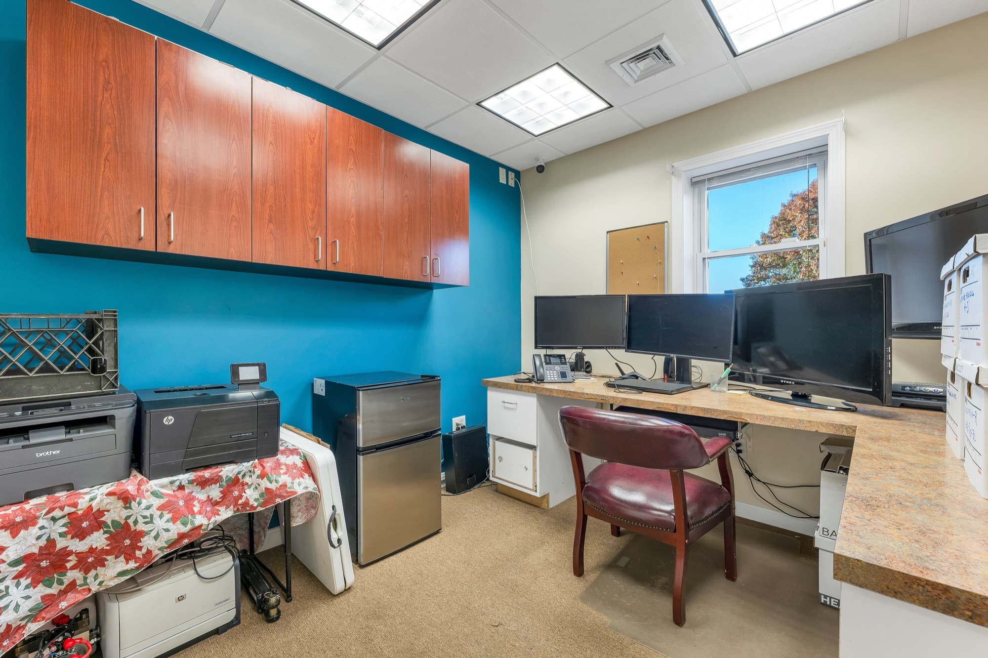 A corner office with cherry upper cabinets, a teal wall, and 3 monitors