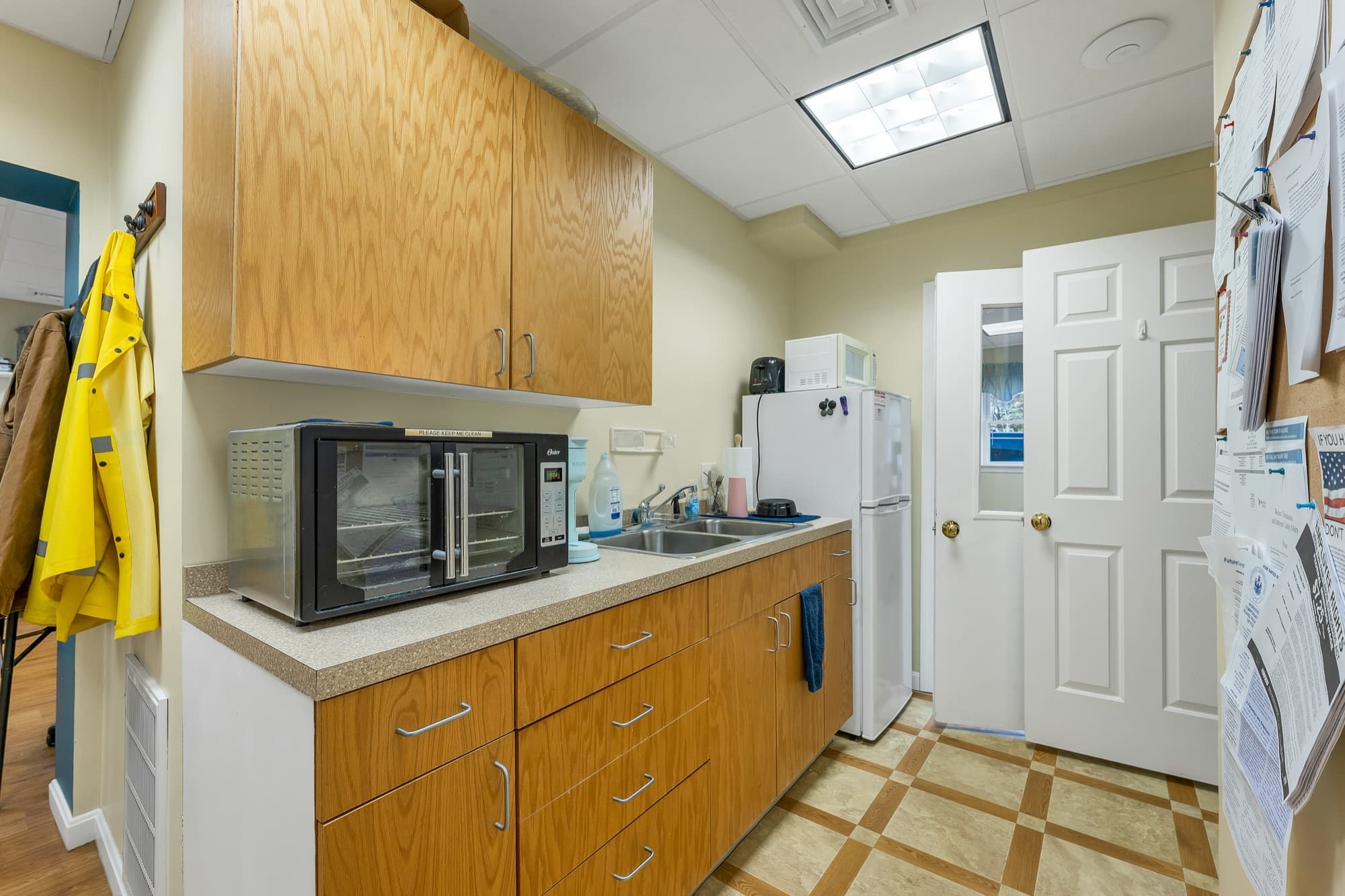 The office kitchenette with oak cabinets, a sink, a microwave, and a refrigerator