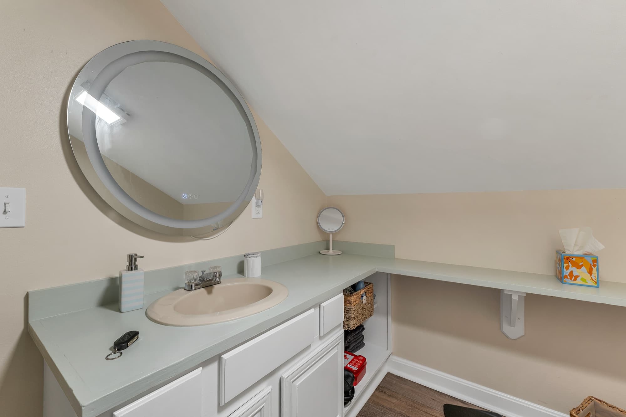 The 2-bedroom apartment's bath with a round mirror and a long vanity under the slope