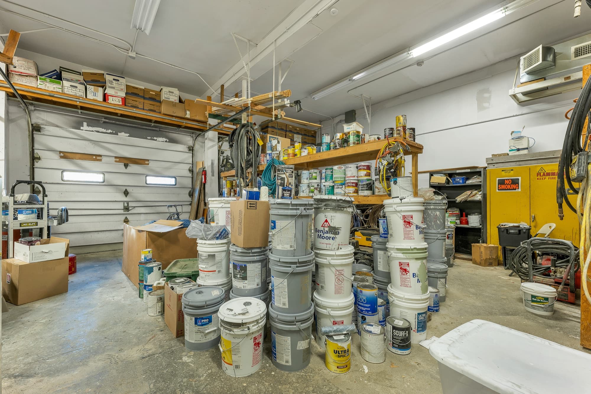 Inside the garage, with 2 of the overhead doors, steel shelving, and the painting equipment